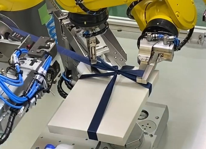 ロボットを使ってリボンを結びます。
アビリカではロボットでも、自動機でも、どちらも対応できますが、この機械ではロボットを使ってリボンを結びました。ロボットでリボンを結ぶ装置は、たぶん世界初です。特許も取得しています。